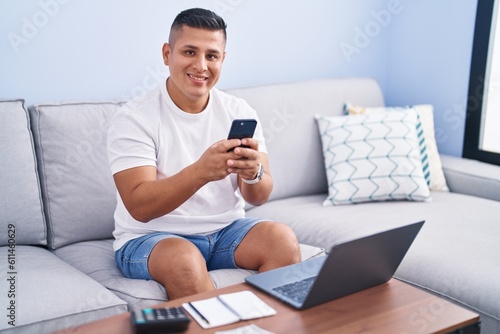 Young latin man using smartphone and laptop at home