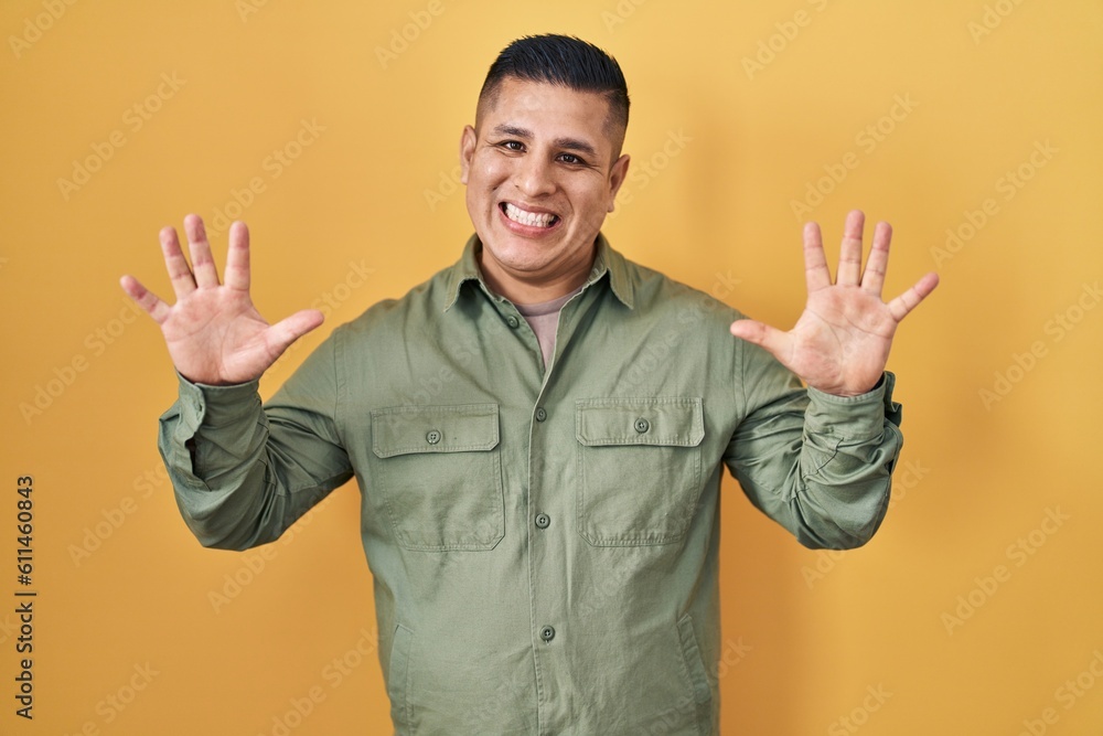 Hispanic young man standing over yellow background showing and pointing up with fingers number ten while smiling confident and happy. Hispanic young man standing over yellow background showing and pointing up with fingers number ten while smiling confident and happy.