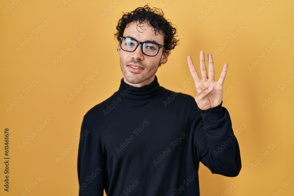Hispanic man standing over yellow background showing and pointing up with fingers number four while smiling confident and happy. Hispanic man standing over yellow background showing and pointing up with fingers number four while smiling confident and happy.