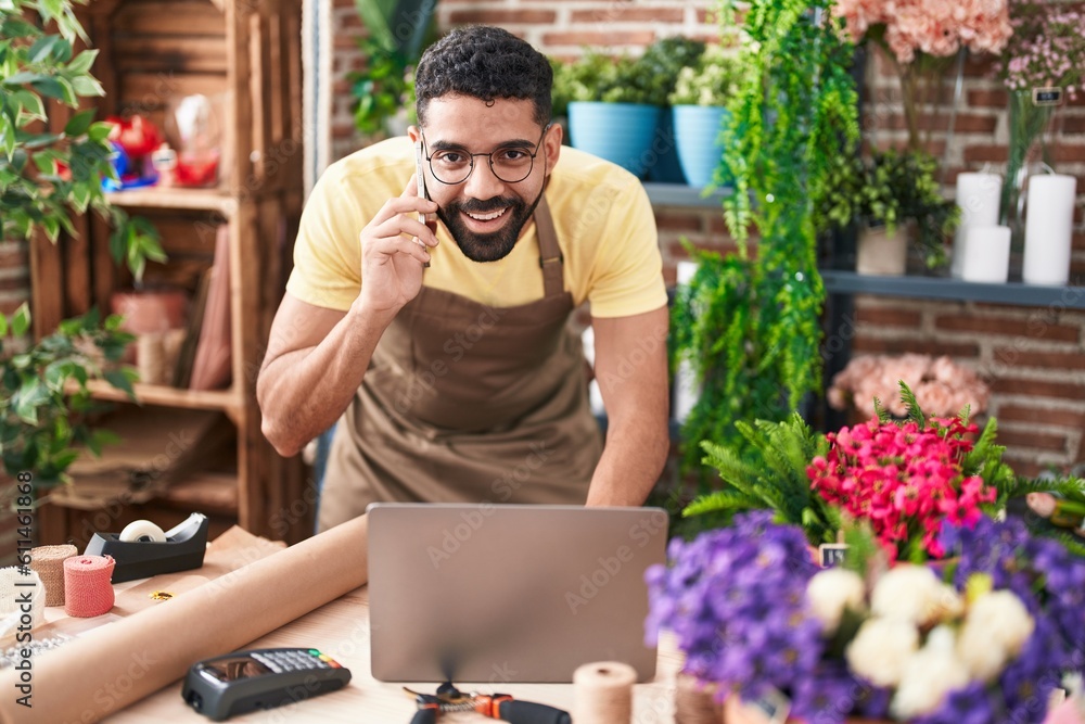 Young arab man florist talking on smartphone using laptop at florist Young arab man florist talking on smartphone using laptop at florist
