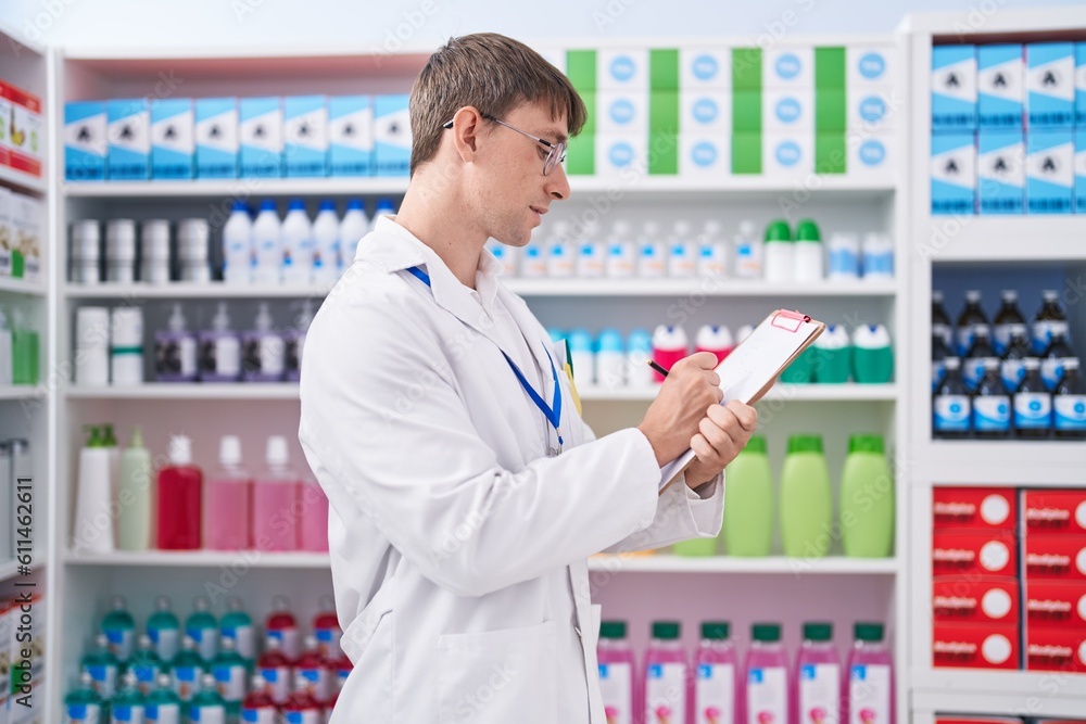 Young caucasian man pharmacist writing on document at pharmacy