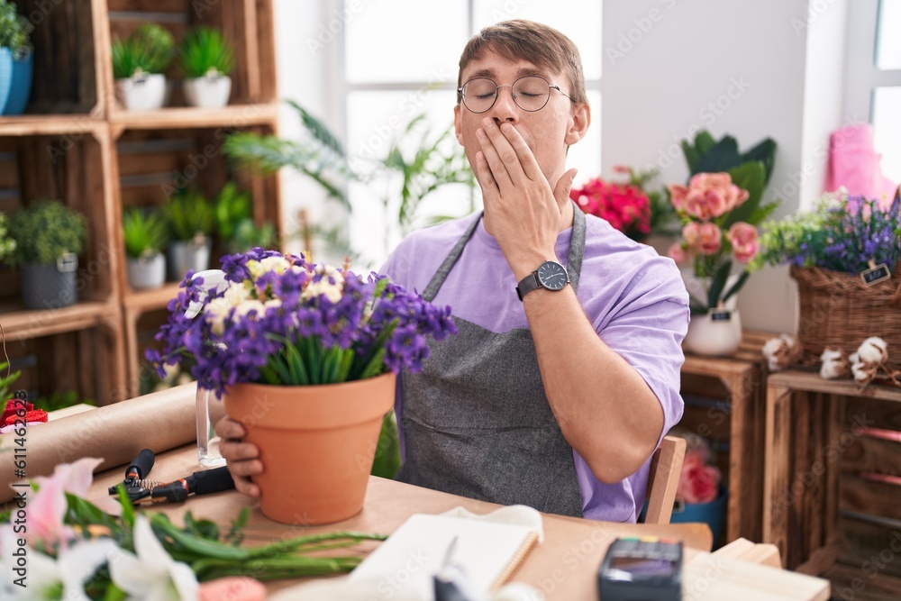 Caucasian blond man working at florist shop bored yawning tired covering mouth with hand. restless and sleepiness.