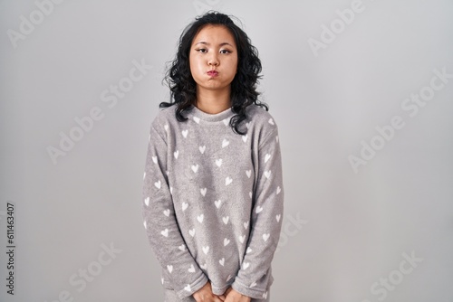 Young asian woman wearing pajama puffing cheeks with funny face. mouth inflated with air  crazy expression.