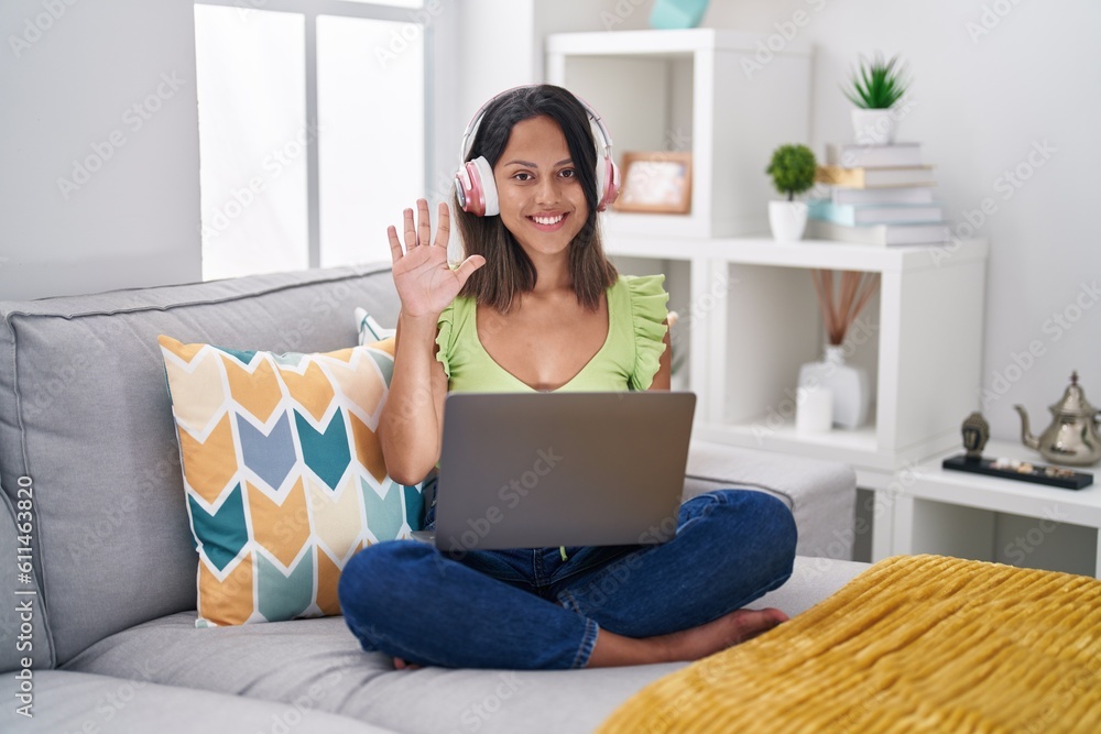 Hispanic young woman using laptop at home showing and pointing up with fingers number five while smiling confident and happy. Hispanic young woman using laptop at home showing and pointing up with fingers number five while smiling confident and happy.