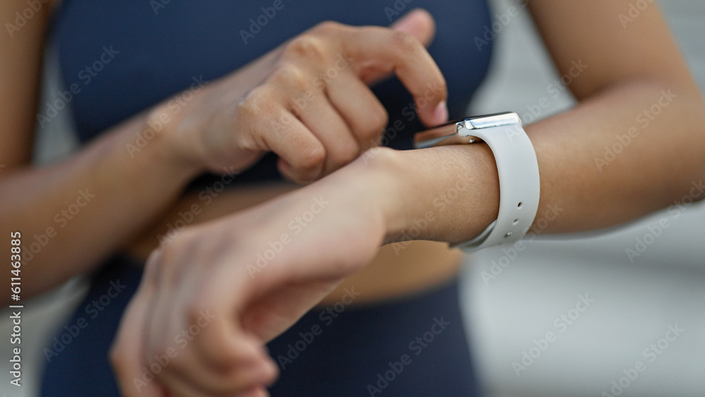 Young beautiful hispanic woman touching smartwatch at street