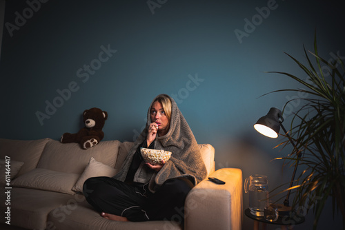 A girl home alone, spellbound by a horror film. Wide-eyed, she leans in, captivated by the flickering TV glow, engrossed in the terrifying narrative. Shadows amplify the suspense, making for an intens