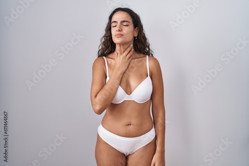 Young hispanic woman wearing white lingerie touching painful neck, sore throat for flu, clod and infection