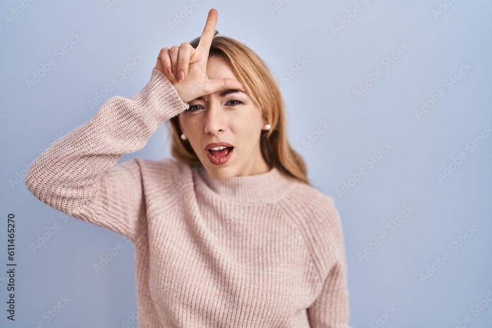 Hispanic woman standing over blue background making fun of people with fingers on forehead doing loser gesture mocking and insulting. Hispanic woman standing over blue background making fun of people with fingers on forehead doing loser gesture mocking and insulting.