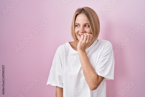 Young caucasian woman standing over pink background looking stressed and nervous with hands on mouth biting nails. anxiety problem.