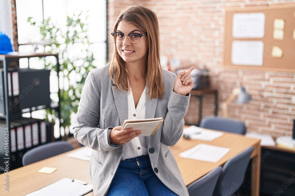 Young hispanic woman working at the office wearing glasses with a big smile on face, pointing with hand finger to the side looking at the camera. Young hispanic woman working at the office wearing glasses with a big smile on face, pointing with hand finger to the side looking at the camera.