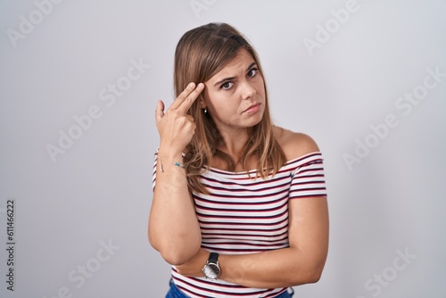 Young hispanic woman standing over isolated background shooting and killing oneself pointing hand and fingers to head like gun, suicide gesture.