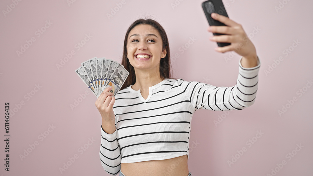 Young beautiful hispanic woman taking selfie holding dollars over isolated pink background Young beautiful hispanic woman taking selfie holding dollars over isolated pink background