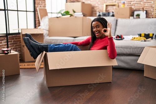 Young african american with braids moving to a new home inside of a cardboard box doing ok sign with fingers, smiling friendly gesturing excellent symbol © Krakenimages.com