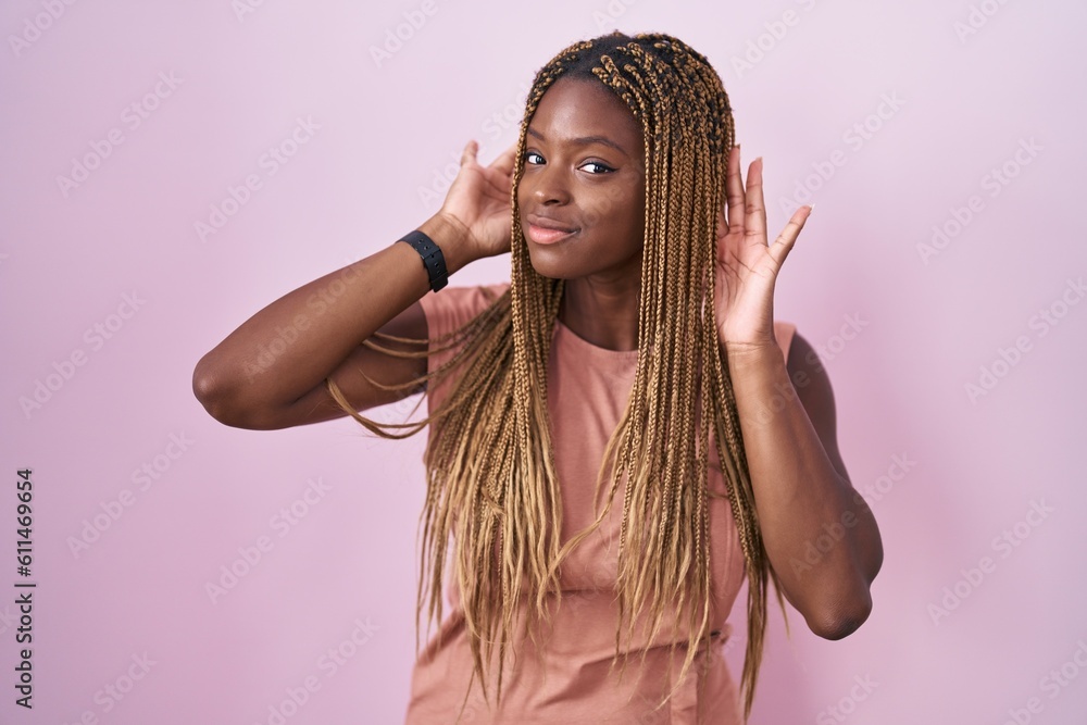 African american woman with braided hair standing over pink background trying to hear both hands on ear gesture, curious for gossip. hearing problem, deaf African american woman with braided hair standing over pink background trying to hear both hands on ear gesture, curious for gossip. hearing problem, deaf