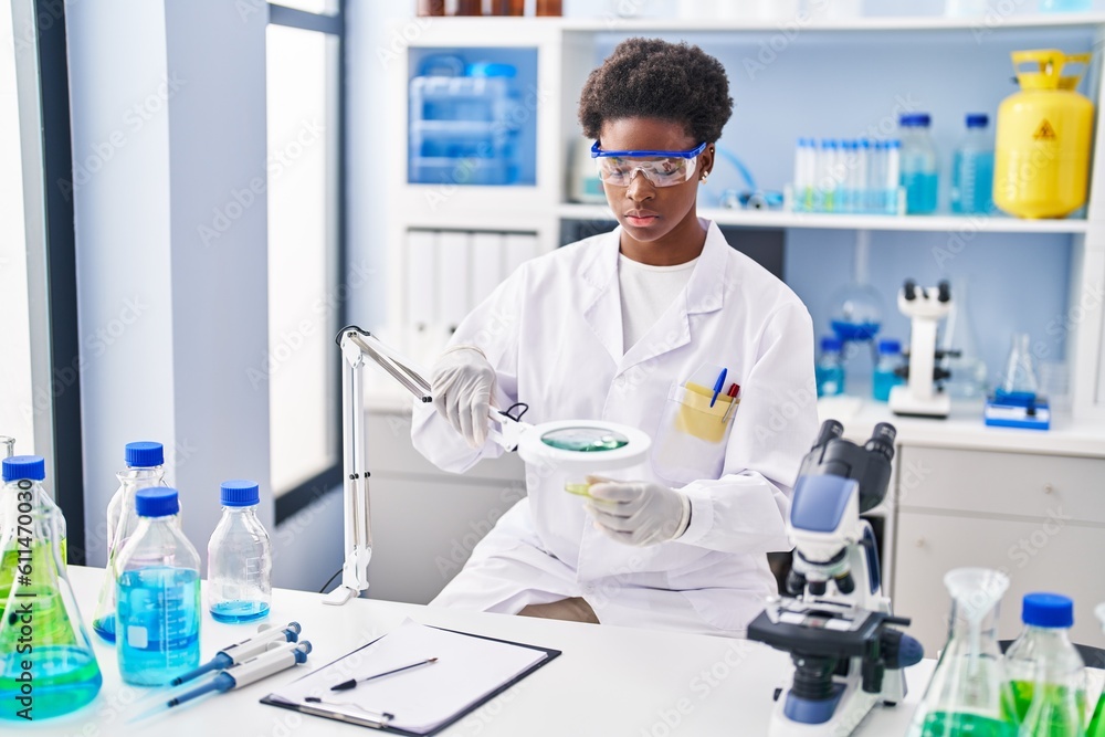 African american woman wearing scientist uniform using magnifying glass at laboratory African american woman wearing scientist uniform using magnifying glass at laboratory
