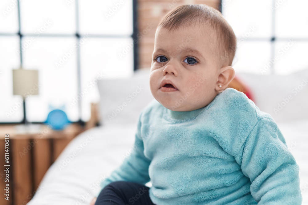 Adorable hispanic baby sitting on bed with relaxed expression at bedroom