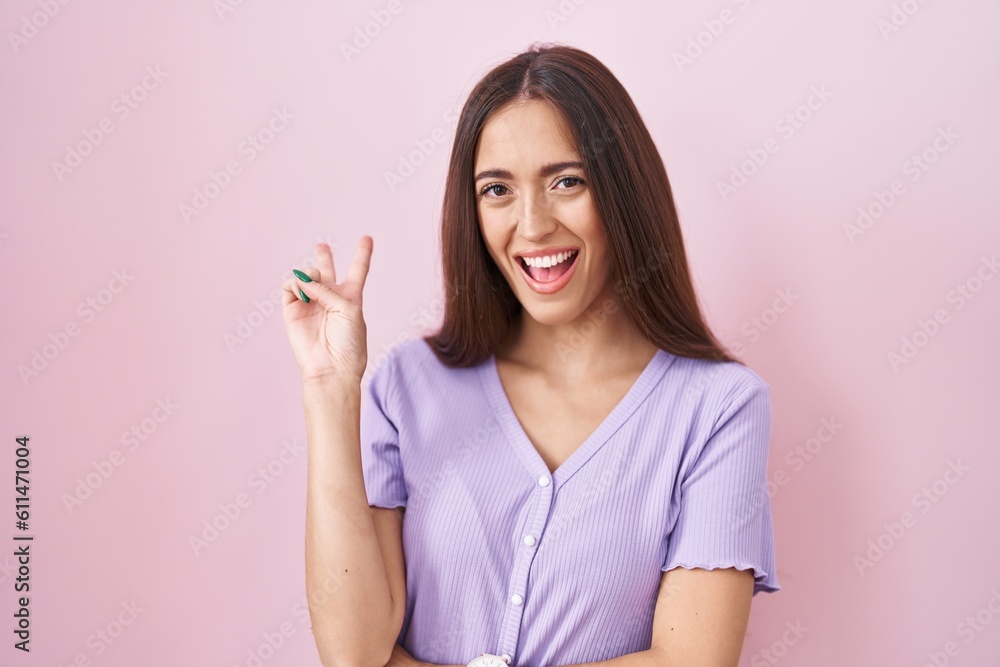 Young hispanic woman with long hair standing over pink background smiling with happy face winking at the camera doing victory sign with fingers. number two. Young hispanic woman with long hair standing over pink background smiling with happy face winking at the camera doing victory sign with fingers. number two.