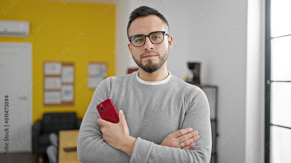 Hispanic man business worker with serious face holding smartphone at office Hispanic man business worker with serious face holding smartphone at office