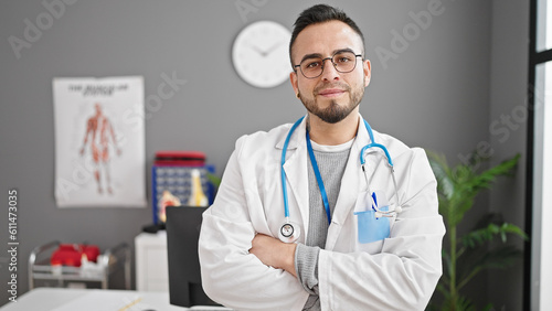 Hispanic man doctor standing with serious expression and crossed arms at the clinic