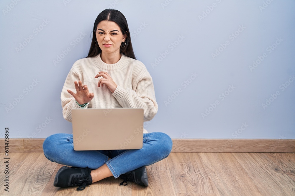 Young woman using laptop sitting on the floor at home disgusted expression, displeased and fearful doing disgust face because aversion reaction. Young woman using laptop sitting on the floor at home disgusted expression, displeased and fearful doing disgust face because aversion reaction.