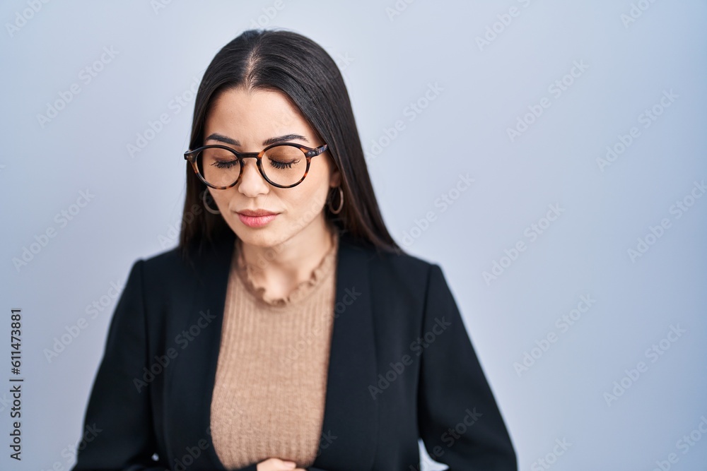 Young brunette woman standing over blue background with hand on stomach because nausea, painful disease feeling unwell. ache concept.