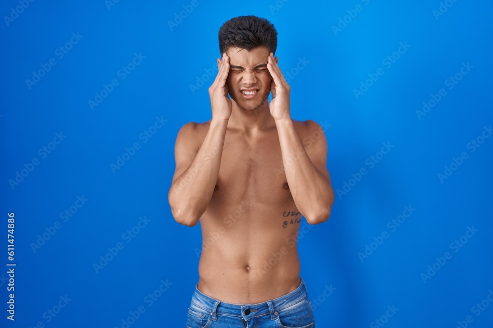 Fototapeta premium Young hispanic man standing shirtless over blue background with hand on head, headache because stress. suffering migraine.