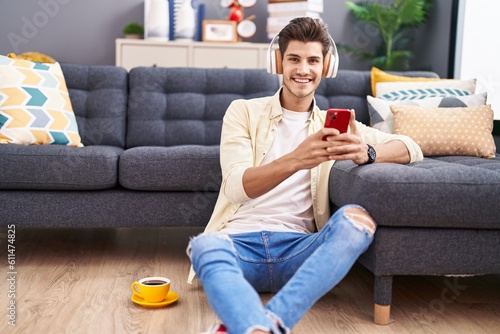 Young hispanic man listening to music sitting on floor at home