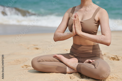 Cropped image of sportswoman sitting in lotus position on sandy beach