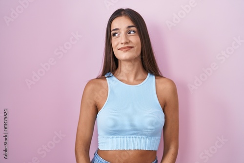 Young brunette woman standing over pink background smiling looking to the side and staring away thinking. © Krakenimages.com