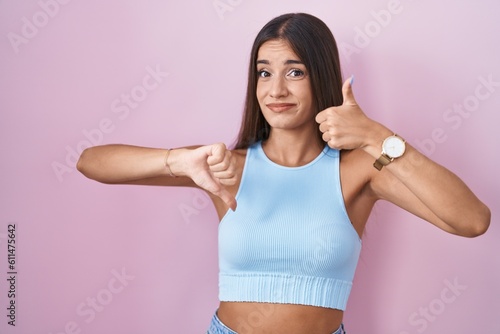 Young brunette woman standing over pink background doing thumbs up and down, disagreement and agreement expression. crazy conflict © Krakenimages.com