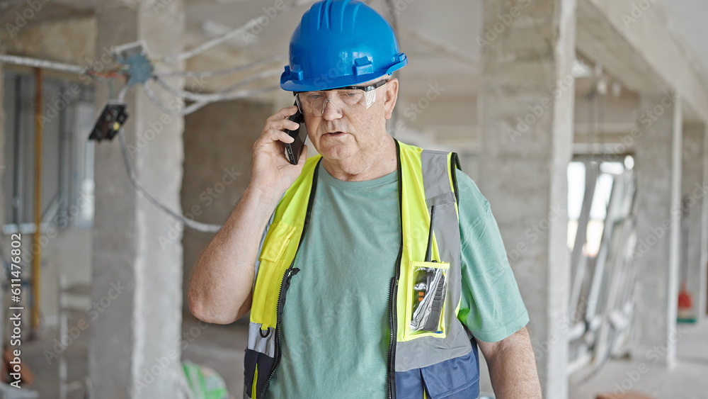 Middle age grey-haired man builder talking on smartphone with relaxed expression at construction site Middle age grey-haired man builder talking on smartphone with relaxed expression at construction site