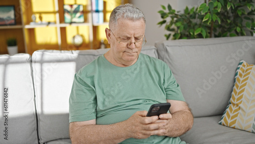 Middle age grey-haired man using smartphone sitting on sofa at home