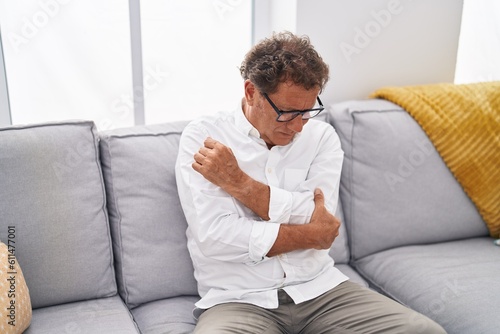 Middle age man suffering for elbow pain sitting on sofa at home