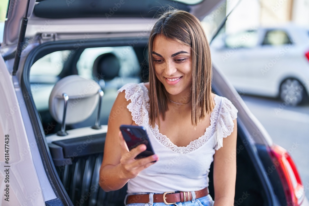 Young beautiful hispanic woman using smartphone sitting on car trunk at street Young beautiful hispanic woman using smartphone sitting on car trunk at street