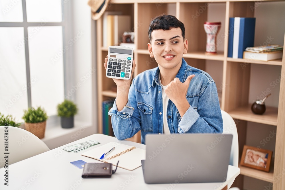 Fototapeta premium Non binary person calculating money savings pointing thumb up to the side smiling happy with open mouth