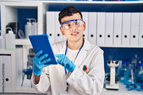 Young non binary man scientist smiling confident using touchpad at laboratory
