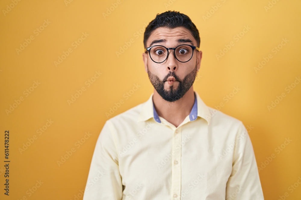 Hispanic young man wearing business clothes and glasses making fish face with lips, crazy and comical gesture. funny expression.