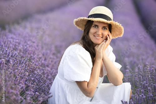 Closeup portrait of beautiful brunette smiling woman 30-35 years old in straw hat and white cotton dress in purple lavender field