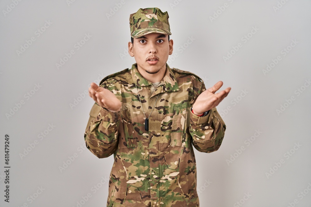 Young arab man wearing camouflage army uniform clueless and confused with open arms, no idea concept. Young arab man wearing camouflage army uniform clueless and confused with open arms, no idea concept.