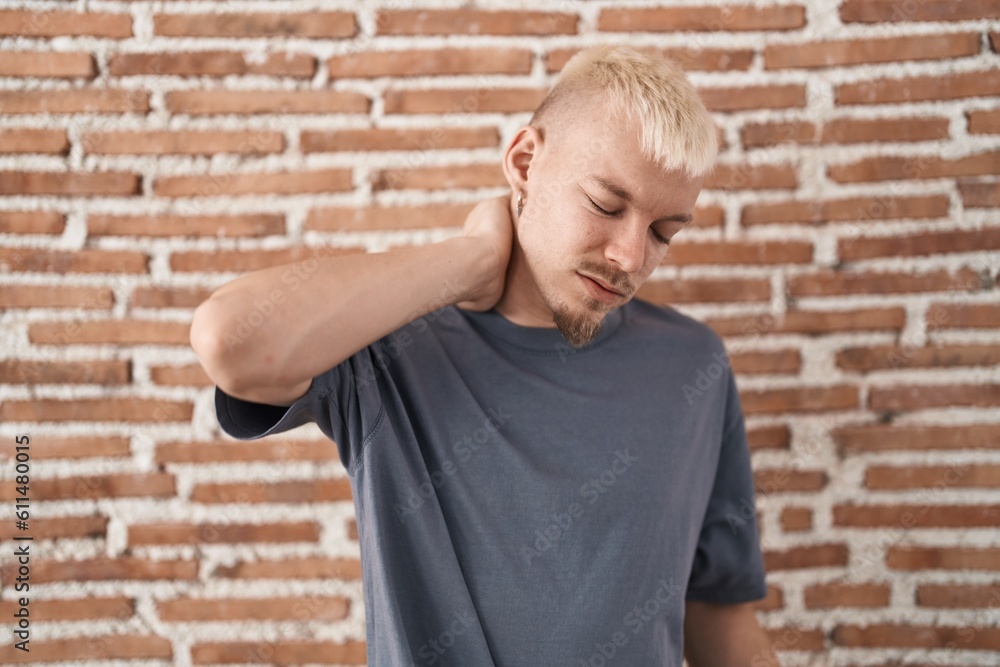Young caucasian man standing over bricks wall suffering of neck ache injury, touching neck with hand, muscular pain Young caucasian man standing over bricks wall suffering of neck ache injury, touching neck with hand, muscular pain