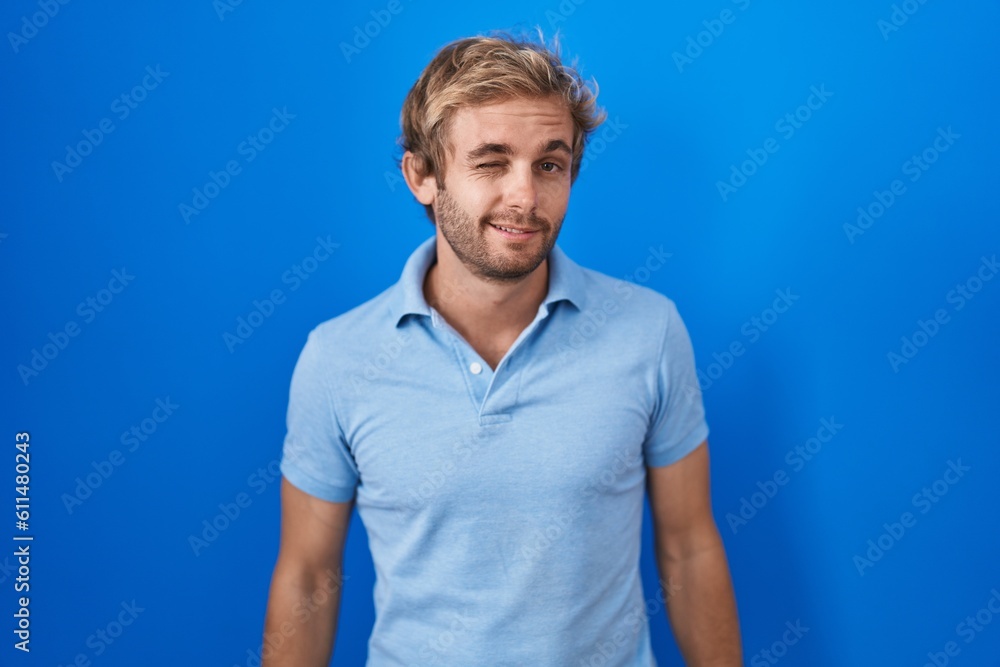 Caucasian man standing over blue background winking looking at the camera with sexy expression, cheerful and happy face. Caucasian man standing over blue background winking looking at the camera with sexy expression, cheerful and happy face.