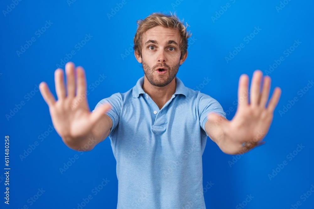 Naklejka premium Caucasian man standing over blue background doing stop gesture with hands palms, angry and frustration expression