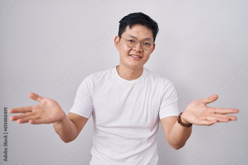 Young asian man standing over white background smiling cheerful offering hands giving assistance and acceptance. Young asian man standing over white background smiling cheerful offering hands giving assistance and acceptance.