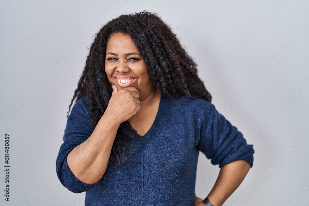 Plus size hispanic woman standing over white background looking confident at the camera with smile with crossed arms and hand raised on chin. thinking positive. Plus size hispanic woman standing over white background looking confident at the camera with smile with crossed arms and hand raised on chin. thinking positive.