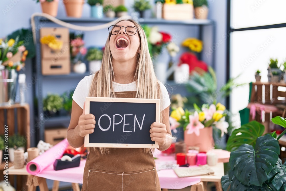 Young blonde woman working at florist holding open sign angry and mad screaming frustrated and furious, shouting with anger looking up. Young blonde woman working at florist holding open sign angry and mad screaming frustrated and furious, shouting with anger looking up.