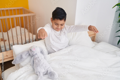 Adorable hispanic boy somnambulist sitting on bed at bedroom photo