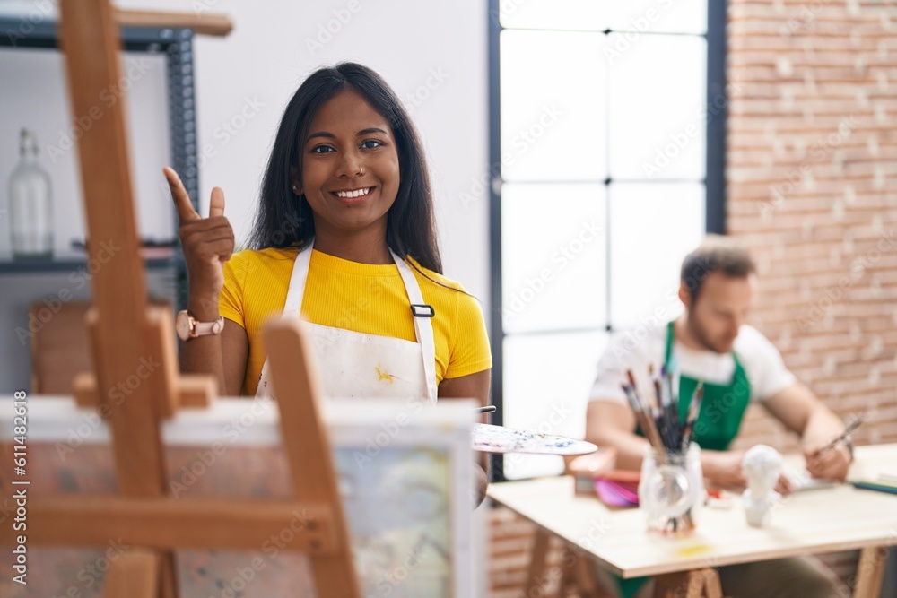 Indian woman at art studio smiling happy pointing with hand and finger to the side Indian woman at art studio smiling happy pointing with hand and finger to the side