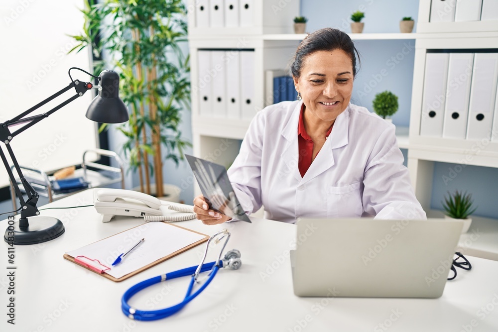 Middle age hispanic woman wearing doctor uniform holding xray at clinic Middle age hispanic woman wearing doctor uniform holding xray at clinic