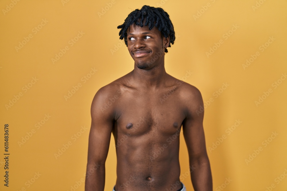 Young african man with dreadlocks standing shirtless smiling looking to the side and staring away thinking.