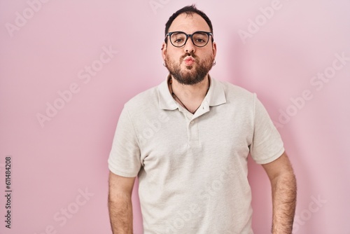 Plus size hispanic man with beard standing over pink background looking at the camera blowing a kiss on air being lovely and sexy. love expression.